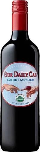 A bottle of Our Daily Cab Cabernet Sauvignon red wine, featuring a dark glass bottle with a red foil capsule and a circular white and red label.