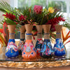 Set of colorful bottles with artistic designs on a table with a floral arrangement in the background.